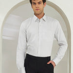Man wearing a white dress shirt and black pants standing in front of an archway.