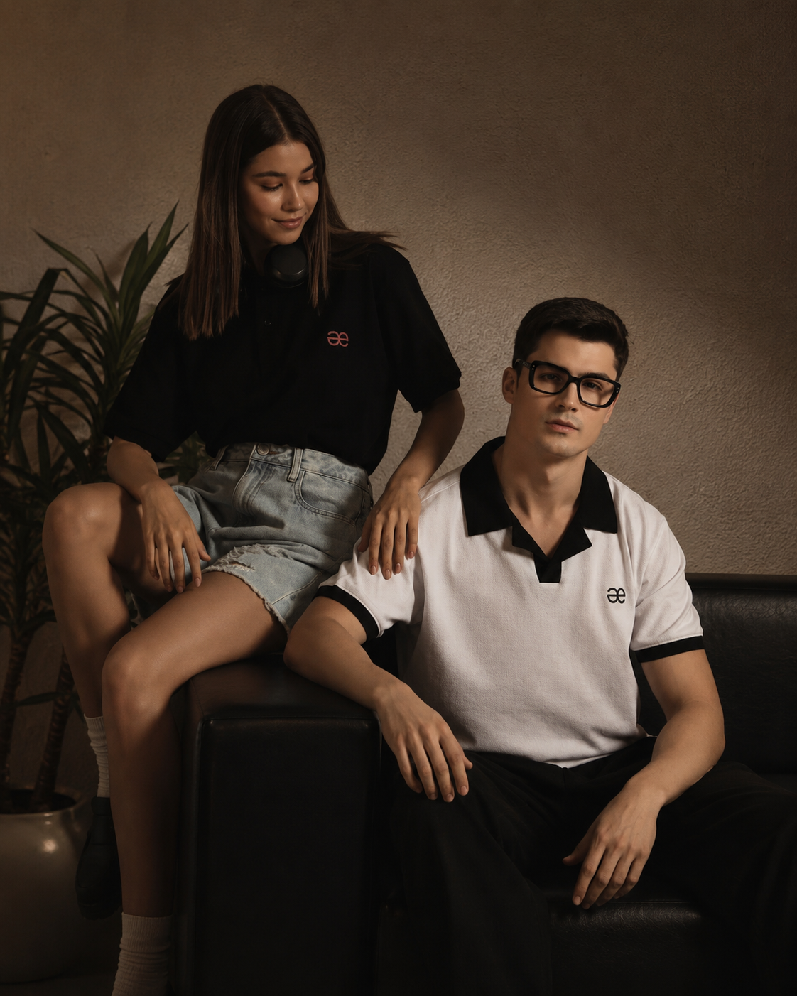 Two models in aeternum premium shirts and polos, sitting on orange sofa, modern style