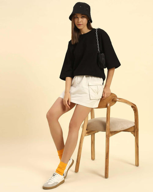 Aeternum Women's Oversized T-Shirt styled with a black bucket hat, white cargo skirt, and yellow socks.