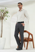 Man wearing a checkered shirt and gray pants standing in a minimalistic room with a plant and chair.
