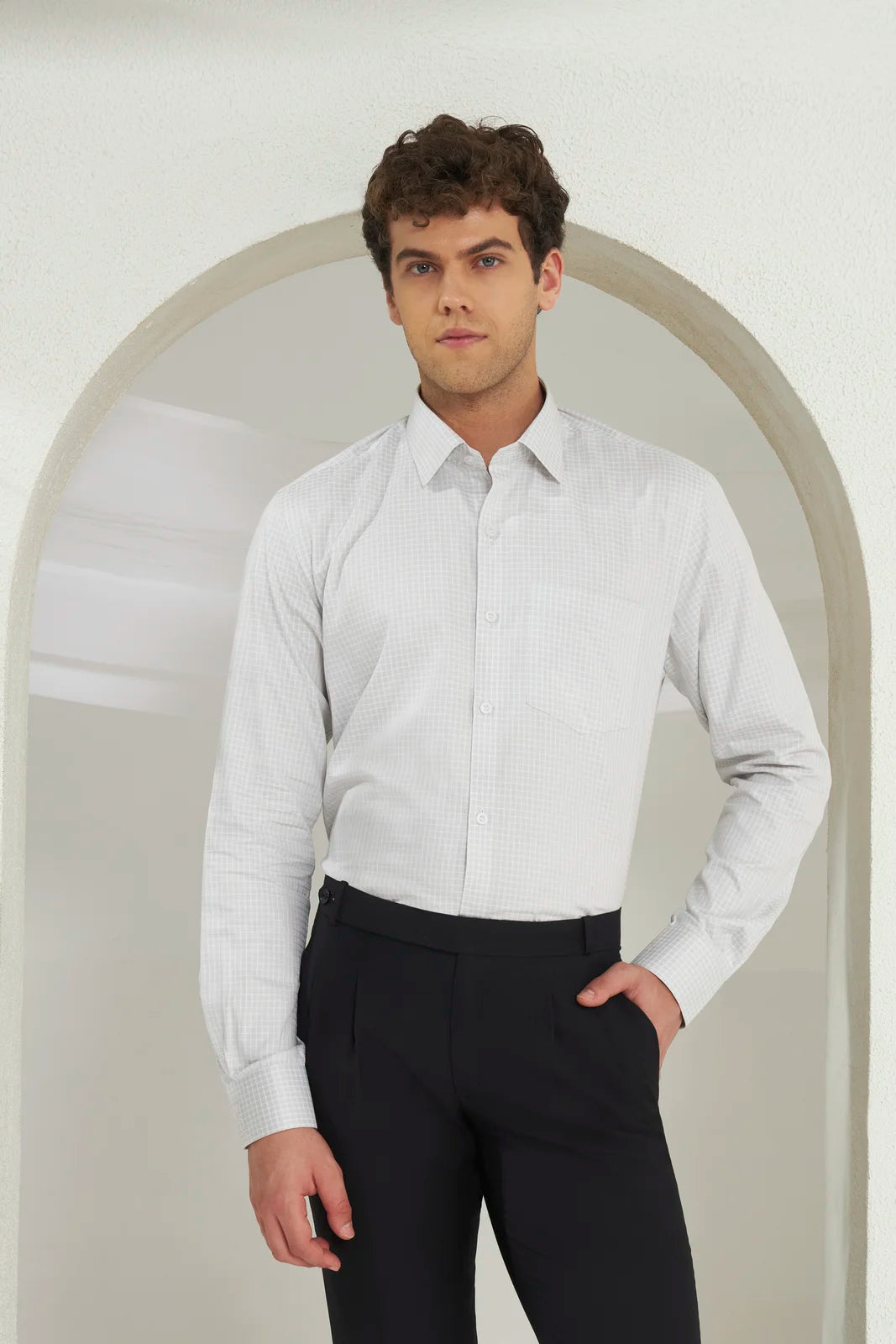 Man wearing a white dress shirt and black pants standing in front of an archway.